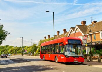 Single decker London bus parked at a bus stop in the city, with passengers waiting to board.