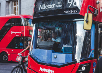 A bus driver sitting at the wheel of a red double-decker bus.